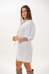 Vestido corto off-white con escote en V, de corte recto y holgado. Cuenta con mangas abullonadas tres cuartos confeccionadas en tejido broderie.