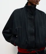 Chaqueta bomber de denim azul oscuro con cuello alto, cierre frontal con zíper y cintura ajustable con cordón. Presenta mangas largas con puños elásticos y bolsillos frontales funcionales.