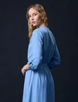 Vestido maxi color beige, con cuello mao y escote en V. Presenta mangas largas con presilla y botón para regular el largo, y un lazo ajustable en la cintura que marca la silueta.