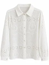 Camisa blanca de manga larga con diseño de broderie y ojales florales, cuello camisero y cierre frontal de botones.