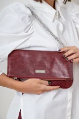 Sobre de mano tipo clutch marca Pecarí, color bordó con textura símil reptil. Cuenta con cierre metálico frontal, solapa plegable y correa de cadena plateada extraíble.