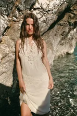 Vestido midi de color beige con escote en pico y tirantes anchos. Presenta un diseño con tejido plisado en la parte superior y aplicaciones de encaje a tono en el escote y la cintura. Cuenta con una tira ajustable con lazada en la espalda y forro interior.