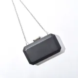 Cartera de mano tipo sobre color negro con textura simil cuero y cierre metálico plateado. Incluye cadena metálica plateada desmontable.