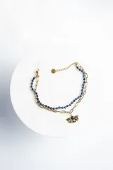 Pulsera dorada de acero quirúrgico con doble cadena, una de eslabones y otra de cuentas azules. Dije colgante de flor con piedra azul en el centro.