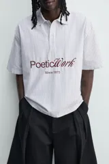 Camisa polo boxy fit de manga corta, confeccionada en tejido de algodón con diseño de rayas verticales celestes y blancas. Cuenta con cuello solapa, cierre frontal con botones y estampado frontal de texto en tono marrón con la leyenda "Poetic Work Since 1975".