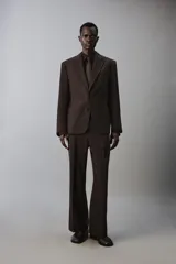 Pantalón de traje flare fit para hombre, confeccionado en tejido con lana, en color marrón oscuro. Presenta tiro medio, trabillas para cinturón, cierre frontal con cremallera y botón, bolsillos laterales y raya central marcada en las perneras.