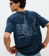 Remera de algodón azul marino con cuello redondo y mangas cortas. Presenta un diseño con estampa minimalista en el frente y una gran ilustración artística del skyline de Nueva York con la frase 'Connected by Movement' en la espalda.