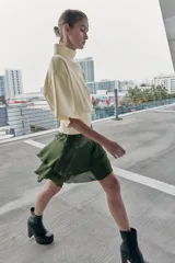 Falda corta de satén color verde oliva, con cintura fruncida y dos niveles de volantes con terminación ondulada.