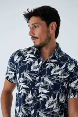 Camisa de manga corta con estampado botánico de hojas en tonos azul y blanco. Presenta cuello clásico, cierre frontal abotonado y corte slim.