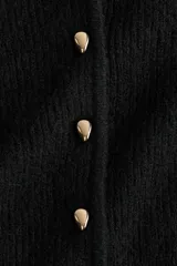 Saco de punto acanalado con cuello redondo, manga larga y cierre frontal con botones metálicos. Presenta un diseño entallado con detalle de peplum en la cintura.