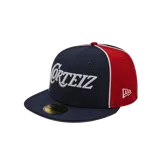 Gorra de béisbol de ala plana, modelo 59 Fifty, colaboración entre Corteiz y New Era. Presenta un diseño tricolor con paneles frontales en azul marino, paneles laterales y traseros en rojo, y detalles en blanco. Incluye el logo de Corteiz bordado en el frente y el logo de New Era en el lateral.