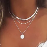 Juego de tres collares plateados de diferentes largos. El más corto es una banda plana, el segundo es una cadena con pequeños brillantes y el tercero es una cadena con un dije redondo con diseño de rayos.