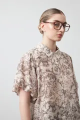 Camisa de manga corta abullonada, con cuello camisero y botones frontales. Presenta un estampado de inspiración barroca en tonos marrón y beige claro.