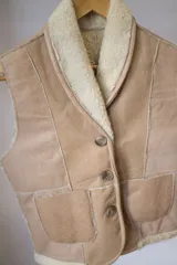 Chaleco de cuero genuino con interior de piel sintética, diseño con cuello solapa, cierre frontal de tres botones y dos bolsillos delanteros aplicados.