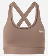 Top deportivo femenino color marrón, con escote redondo y tiras elásticas cruzadas en la espalda. Presenta un pequeño logo bordado en el centro del busto.
