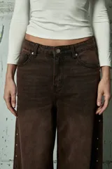 Jean de corte wide leg en color gris lavado, con diseño de aberturas laterales decoradas con tachas metálicas a lo largo de toda la pierna.