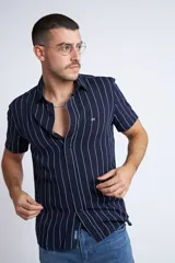 Camisa de manga corta con diseño a rayas verticales en color azul marino y blanco. Presenta cuello clásico, cartera abotonada frontal y logo bordado en el pecho. Posee un corte slim fit.