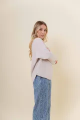Buzo tejido de punto en color beige, con cuello redondo, mangas largas y silueta relajada con dobladillo irregular, siendo más largo en la parte trasera.