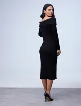 Vestido midi de punto rib, color negro, con escote bote y cuello volcado. Presenta mangas largas y un diseño ajustado al cuerpo con tajo lateral en el ruedo.