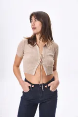 Top corto de tejido de punto color beige, con cuello polo, mangas cortas y cierre frontal con cordones.