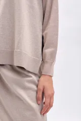 Buzo de tejido de punto color beige con hilo de lurex que le da un brillo sutil. Presenta cuello redondo, mangas largas y un calce holgado.