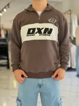 Hoodie de corte clásico con medio cierre y cuello alto, en color marrón con una franja horizontal blanca en el pecho que incluye el logo estampado en negro. Presenta además un pequeño bordado en el hombro izquierdo y puños y cintura elastizados de rib.