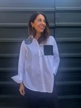 Camisa blanca de corte clásico con bordado de hilo negro en el hombro y bolsillo de cuerina negro en el pecho.