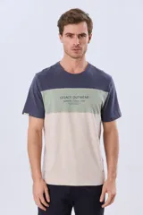 Remera de manga corta con diseño de bloques de color en tonos gris, blanco y azul marino. Cuenta con cuello redondo y una estampa tipográfica en el centro del pecho.
