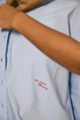 Camisa oversize de popelina 100% algodón, color celeste, con estampado en serigrafía en la parte trasera y en el bolsillo delantero.