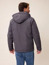 Campera de nylon gris con capucha, cierre frontal completo y bolsillos laterales. Presenta un diseño minimalista con logo bordado en el pecho.