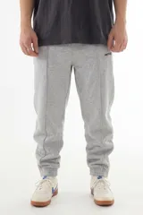 Pantalón de jogging gris melange con costuras frontales marcadas, cintura elástica y cierres en los tobillos. Presenta el logo de la marca bordado en la pierna izquierda.