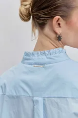 Camisa de algodón color celeste, con cuello mao y puños con detalle de volados. Presenta cierre frontal oculto con botones y un diseño de corte clásico.