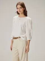 Blusa blanca con cuerpo delantero y mangas de lino, espalda de algodón con elastano, cuello redondo y mangas largas abullonadas con puños elásticos. Presenta un pequeño detalle bordado en la parte superior del pecho.