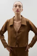 Camisa de manga larga color marrón con textura arrugada, cuello clásico y cierre frontal mediante lazos para anudar.