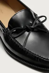 Mocasín de vestir fabricado en piel con acabado brillante. Presenta un detalle de lazo en el empeine, plantilla de piel y suela a contraste con un ligero tacón.
