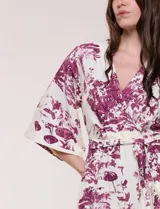 Enterito largo de calce fluido con escote en V cruzado, mangas 3/4 anchas, cintura elastizada con lazo ajustable y pantalón wide leg con bolsillos laterales. Estampado tipo toile de Jouy en tonos violeta sobre fondo blanco.
