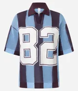 Remera de punto con diseño sportcore, cuello polo y mangas cortas amplias. Presenta un patrón de rayas verticales en tonos azul y bordó, con el número 82 estampado en el frente.