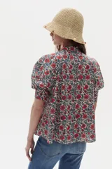 Camisa blanca de algodón con cuello mao, botonera oculta, mangas cortas estilo raglán con cortes estructurados y un bolsillo frontal con cierre.