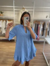 Vestido corto de lino 100% color celeste claro, con escote en V y cuello mao. Tiene mangas cortas y un ruedo con volados.