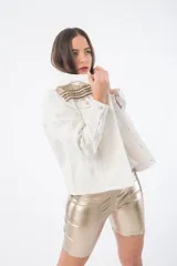 Campera de jean color crudo con cuello alto y apliques de galones dorados y plateados en cuello y hombros.