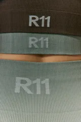 Legging deportiva de tiro alto confeccionada en tejido seamless (sin costuras) con textura acanalada. Presenta un diseño ajustado al cuerpo y logo R11 en la parte trasera de la cintura.