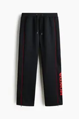 Pantalón jogger negro de corte relajado, con cordón ajustable en la cintura, franjas laterales rojas y estampado con la palabra "Honda" en la pierna izquierda.