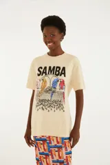Remera beige de algodón con diseño estampado frontal que incluye la palabra "Samba" y cuatro loros de colores.