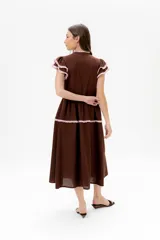 Vestido midi de lino blanco con diseño de broderie, cuello alto, cierre frontal con botones y volados decorativos en los hombros y el cuerpo.