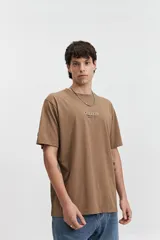 Remera de manga corta color gris oscuro, con escote redondo y ajuste regular. Presenta un estampado frontal con el texto "MISTRAL KAMIOKA NEW TRIAL SINCE 1976 // NLD".