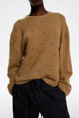 Sweater de punto en color gris oscuro, con corte boxy y escote en caja. Presenta mangas largas rectas y está decorado con pequeños remaches plateados distribuidos por toda la prenda. Confeccionado en una mezcla de lana y alpaca que aporta calidez.