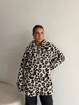 Buzo de peluche con estampado animal print, cuello alto con cierre frontal parcial y detalle de etiqueta decorativa en el pecho.