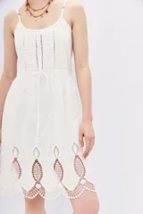 Vestido blanco de algodón con tirantes finos, escote con detalles fruncidos y bordados calados en el ruedo.