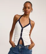 Top de tejido rib blanco, ajustado al cuerpo, con escote profundo y cuello halter. Presenta un ribete contrastante azul marino en el escote y a lo largo del cierre frontal de botones.