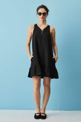 Vestido corto de lino color negro, con silueta suelta, escote en V, botón decorativo, bolsillos laterales y volado en el ruedo.
